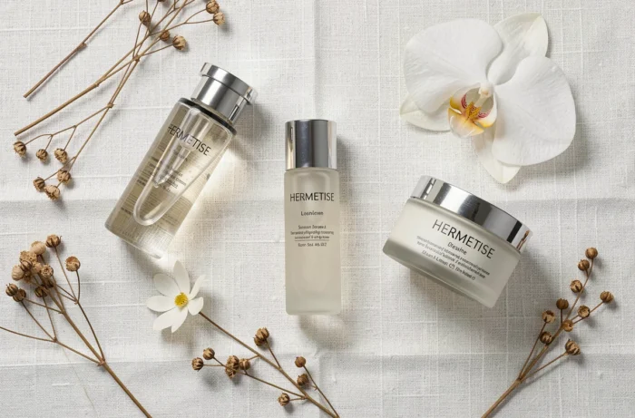 Flat lay élégant des produits de soin Hermetise sur lin blanc avec fleurs séchées et orchidée, esthétique luxe